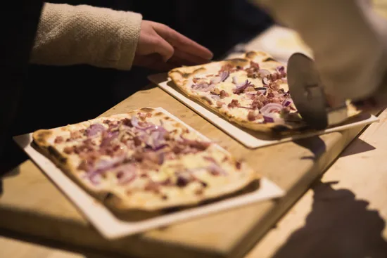 Freshly baked Flammkuchen with bacon and red onions being sliced on wooden counter